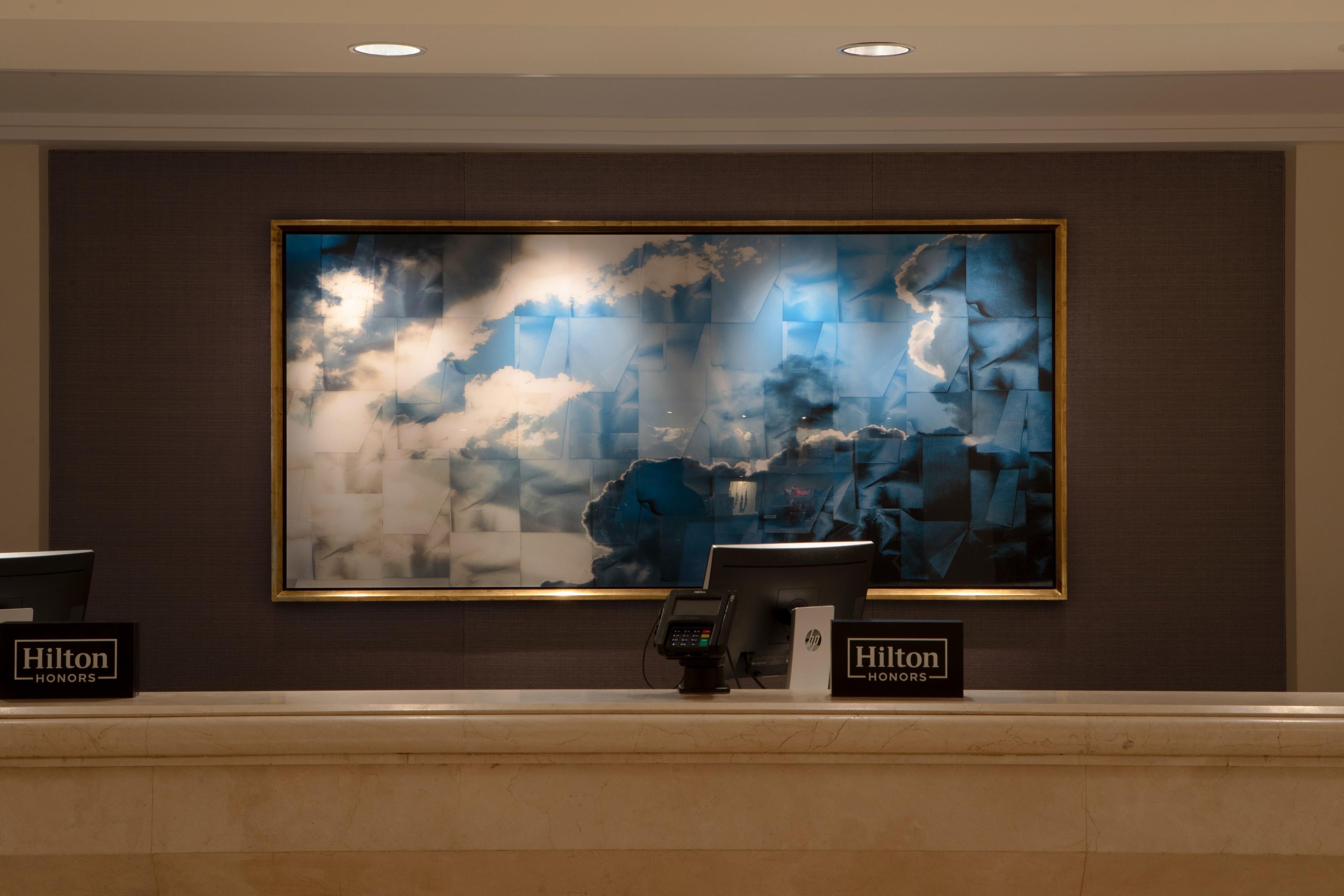 A reception desk with a large abstract painting above it, two 'Hilton Honors' plaques, and a modern design with a marble countertop.