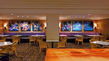 A restaurant with booths, tables, and chairs. There are wall-mounted screens displaying cityscapes.