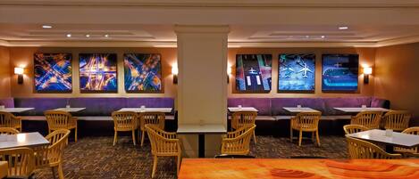 A restaurant with booths, tables, and chairs. There are wall-mounted screens displaying cityscapes.