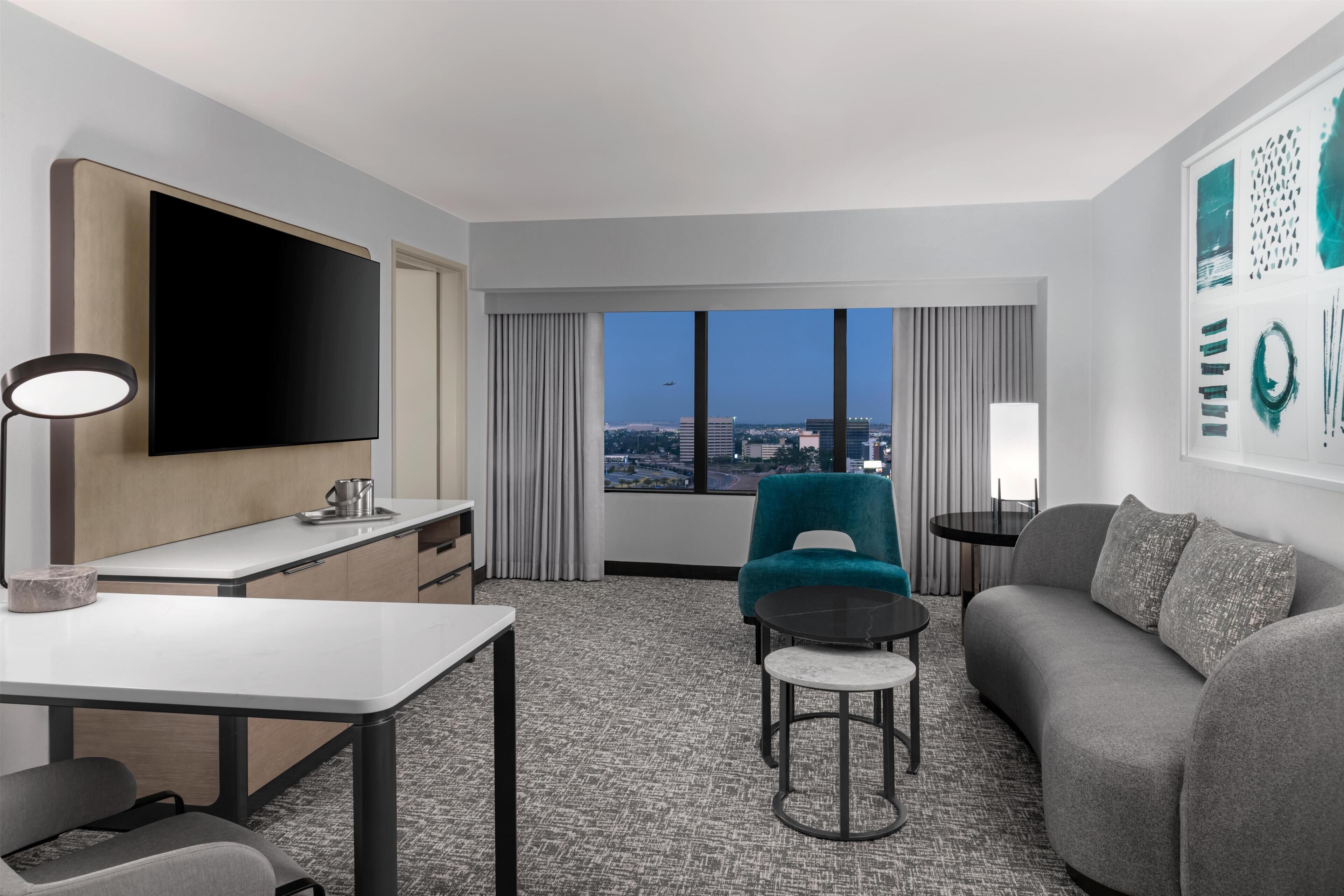 A modern hotel room with a flat-screen TV, a dining table, a sofa, and a chair.