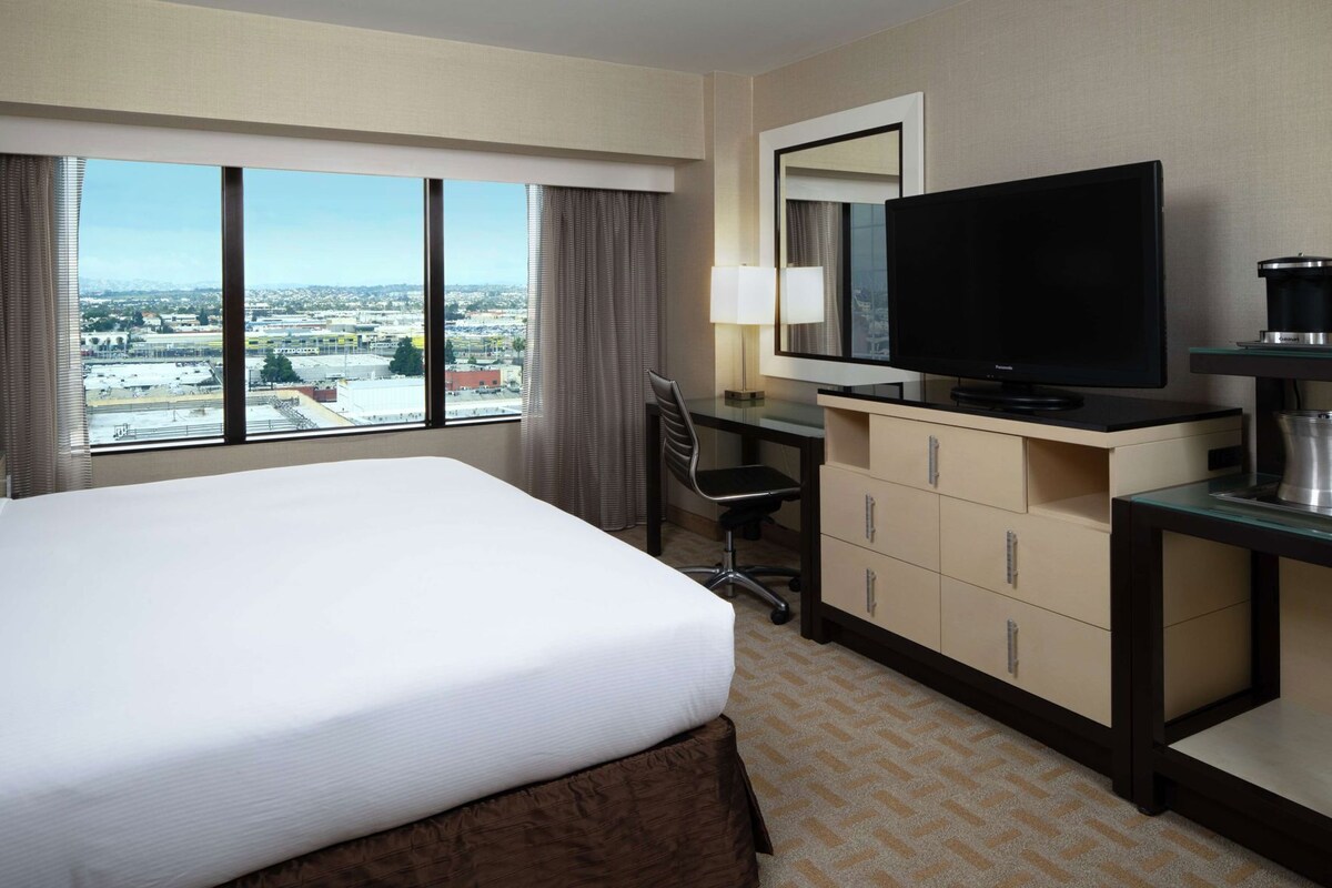 Een hotelkamer met een groot bed, een bureau met een computer, een televisie en een koffiezetapparaat.