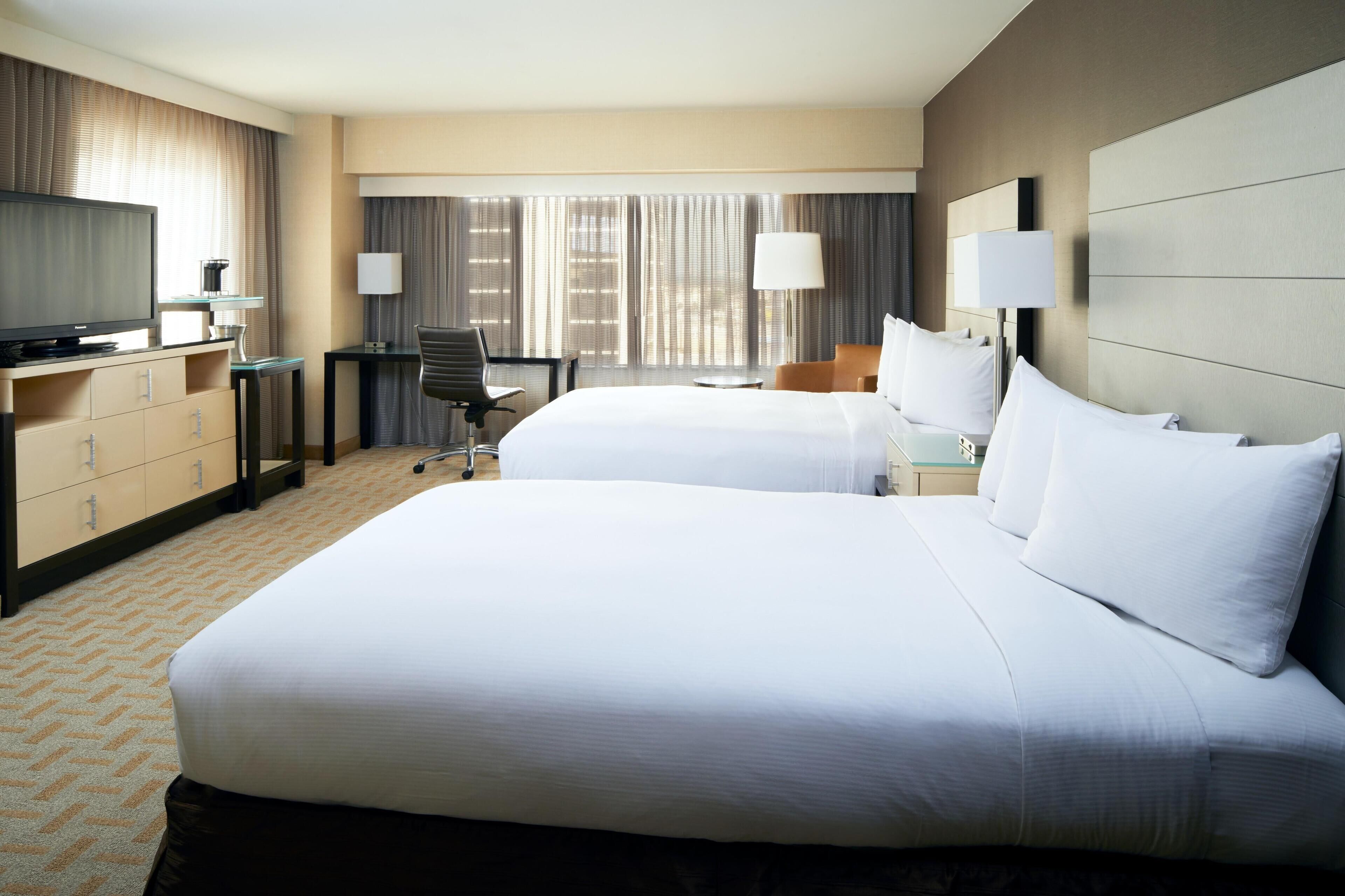 Une chambre d’hôtel avec deux lits, un bureau, une chaise, une télévision et un mini-bar.