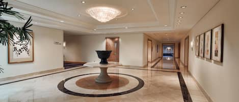 A spacious hallway with a central table, framed artwork on the walls, and a chandelier.
