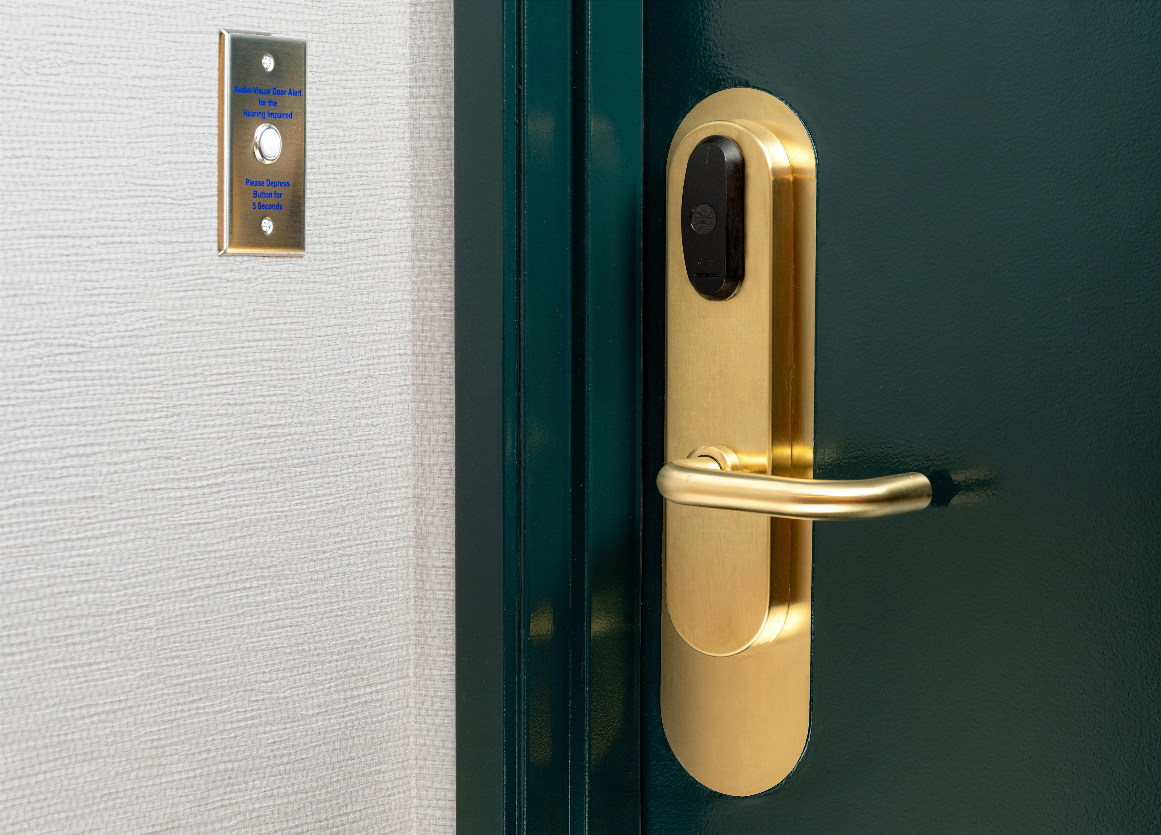 Puerta con manija dorada y botón de alerta visual para personas con discapacidad auditiva.