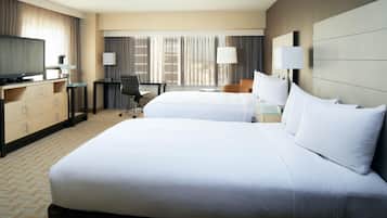 A hotel room with two beds, a desk, a chair, a television, and a minibar.