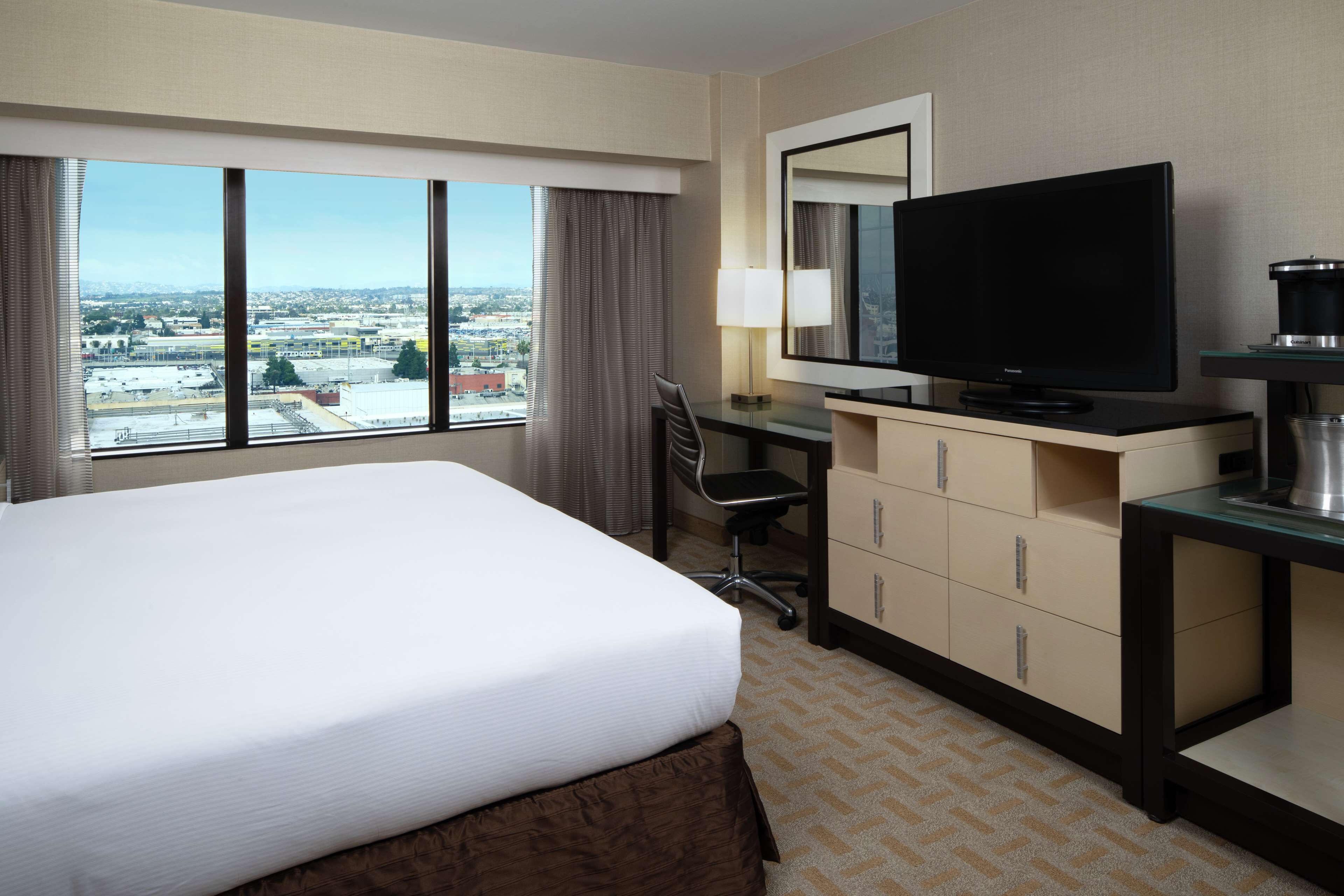 A hotel room with a large bed, a desk with a television, a coffee maker, and a view of the city.