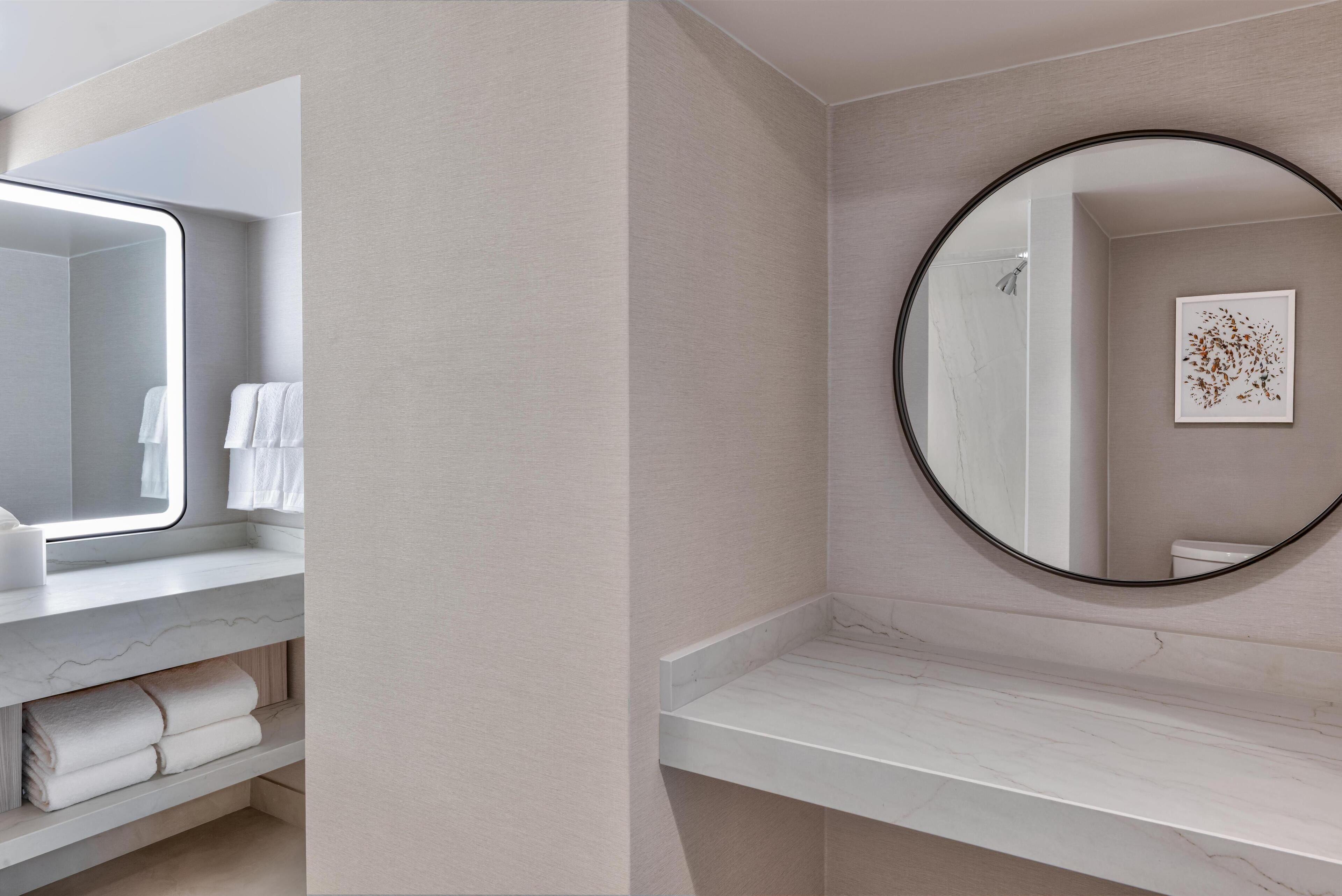 Een moderne badkamer met een marmeren wastafelmeubel, een grote spiegel en een ronde spiegel aan de muur.