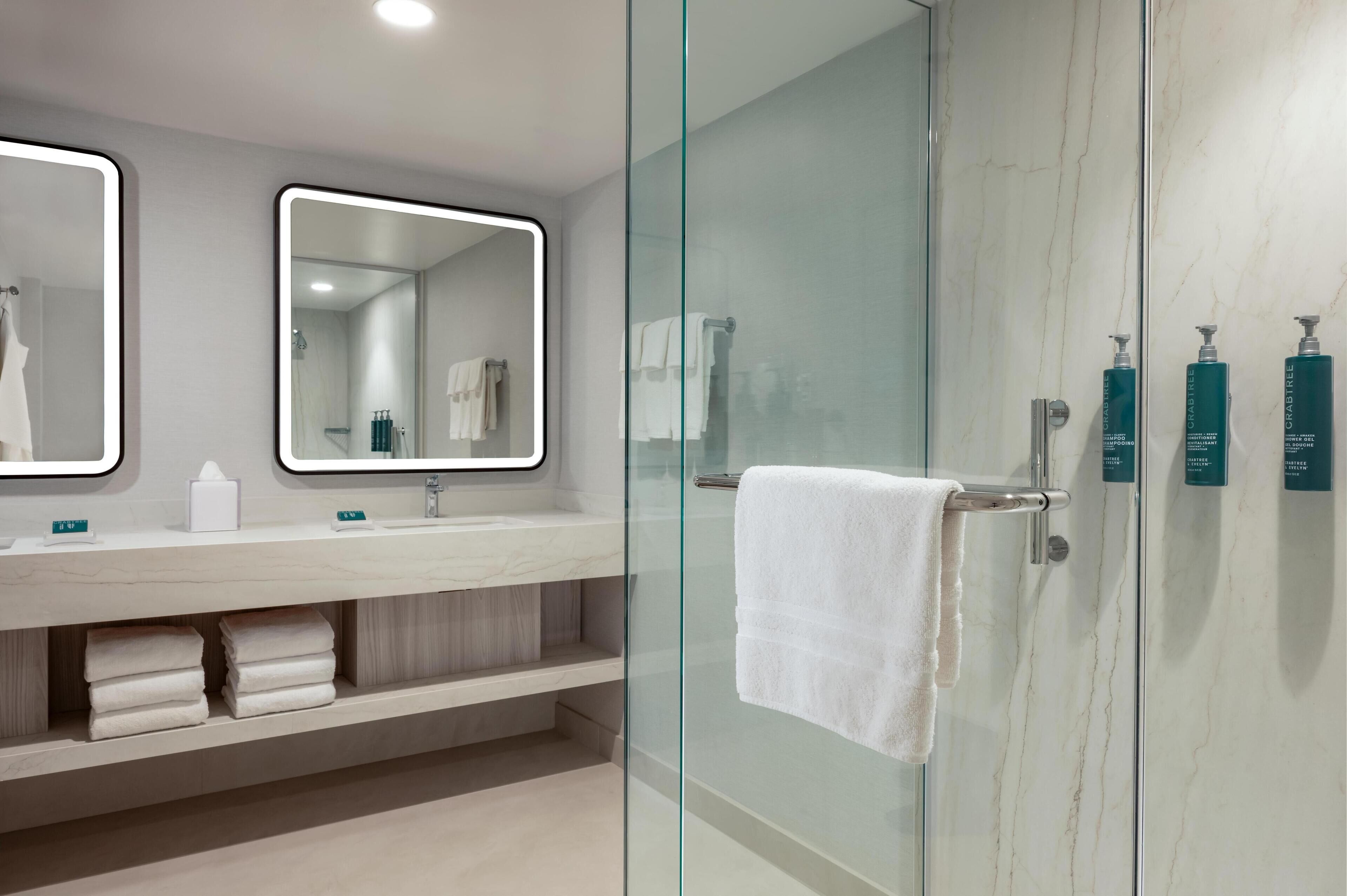 A modern bathroom with two mirrors, a glass shower enclosure, and a towel rack.