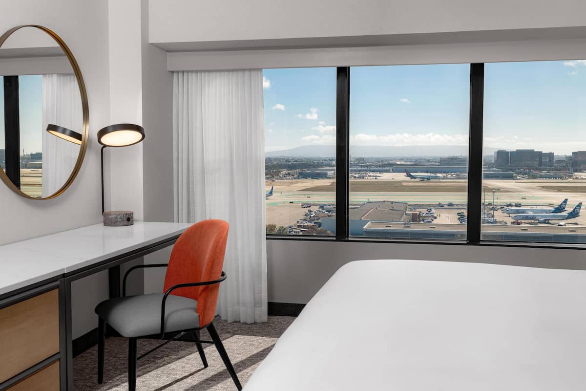A hotel room with a large window offering a view of an airport and cityscape.