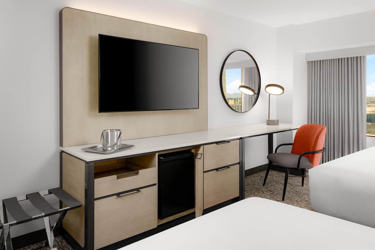 A hotel room with a flat-screen TV mounted on the wall, a desk with a coffee maker, a chair, and a bed.