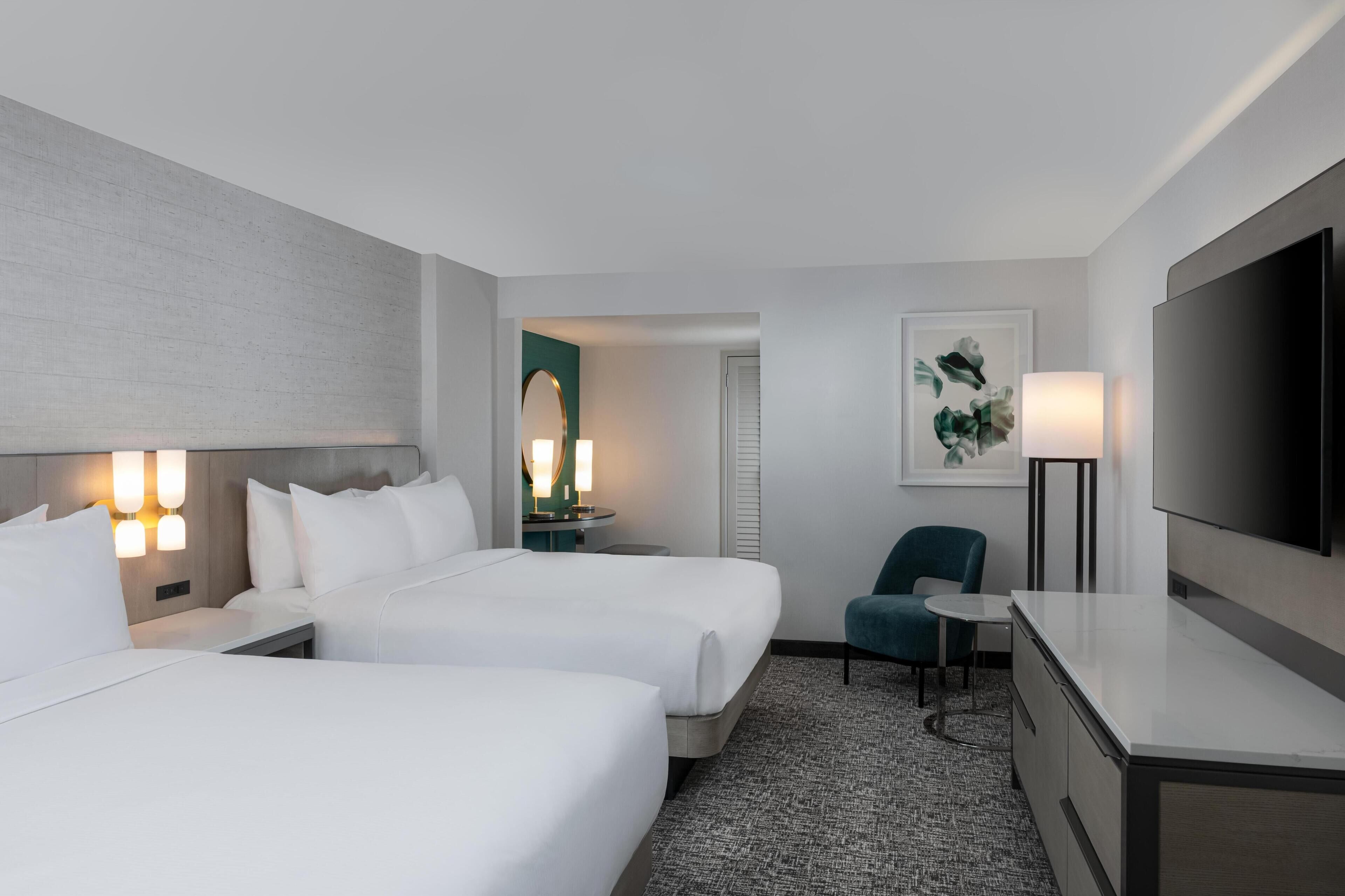 A hotel room with two beds, a TV, a desk, and a chair.