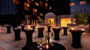 An outdoor terrace with tables set for dining, surrounded by a modern building with large windows and a well-lit entrance. - Hilton Los Angeles Airport (Los Angeles)