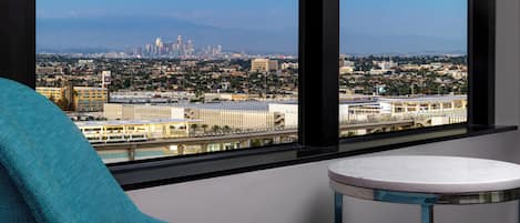 A room with a large window offering a cityscape view, a blue armchair, and a small round table.