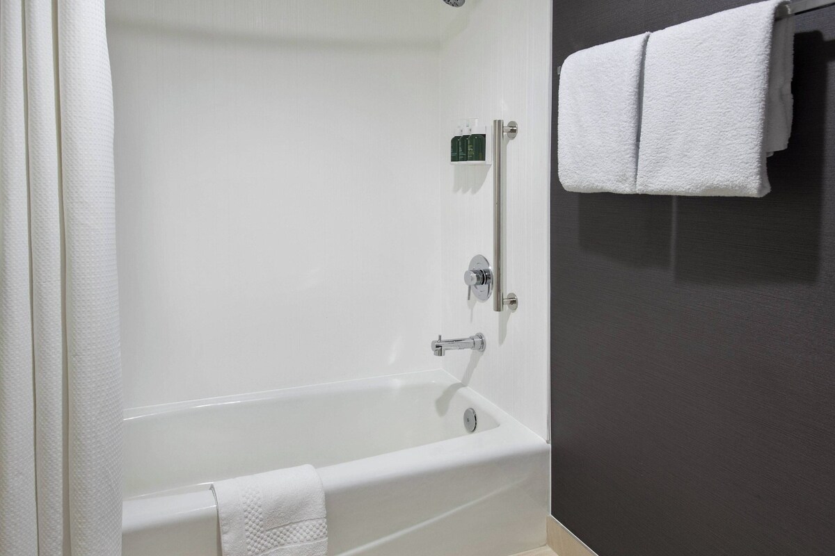 Una bañera blanca con toalla, panel de control y toallero frente a una pared oscura.