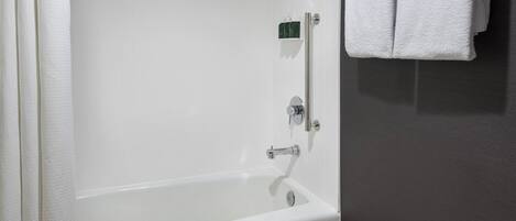 A white bathtub with a towel, a control panel, and a towel rack against a dark wall.