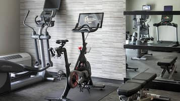 A gym with cardio equipment, a mirrored wall, and a TV screen displaying workout classes.