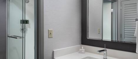 A modern bathroom with a glass-enclosed shower, a white sink with a sleek faucet, and a large mirror.