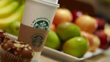 A Starbucks cup with a muffin and a plate of apples.