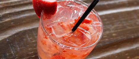 A glass with a strawberry garnish and a straw, filled with a pinkish beverage and ice cubes, on a wooden surface.