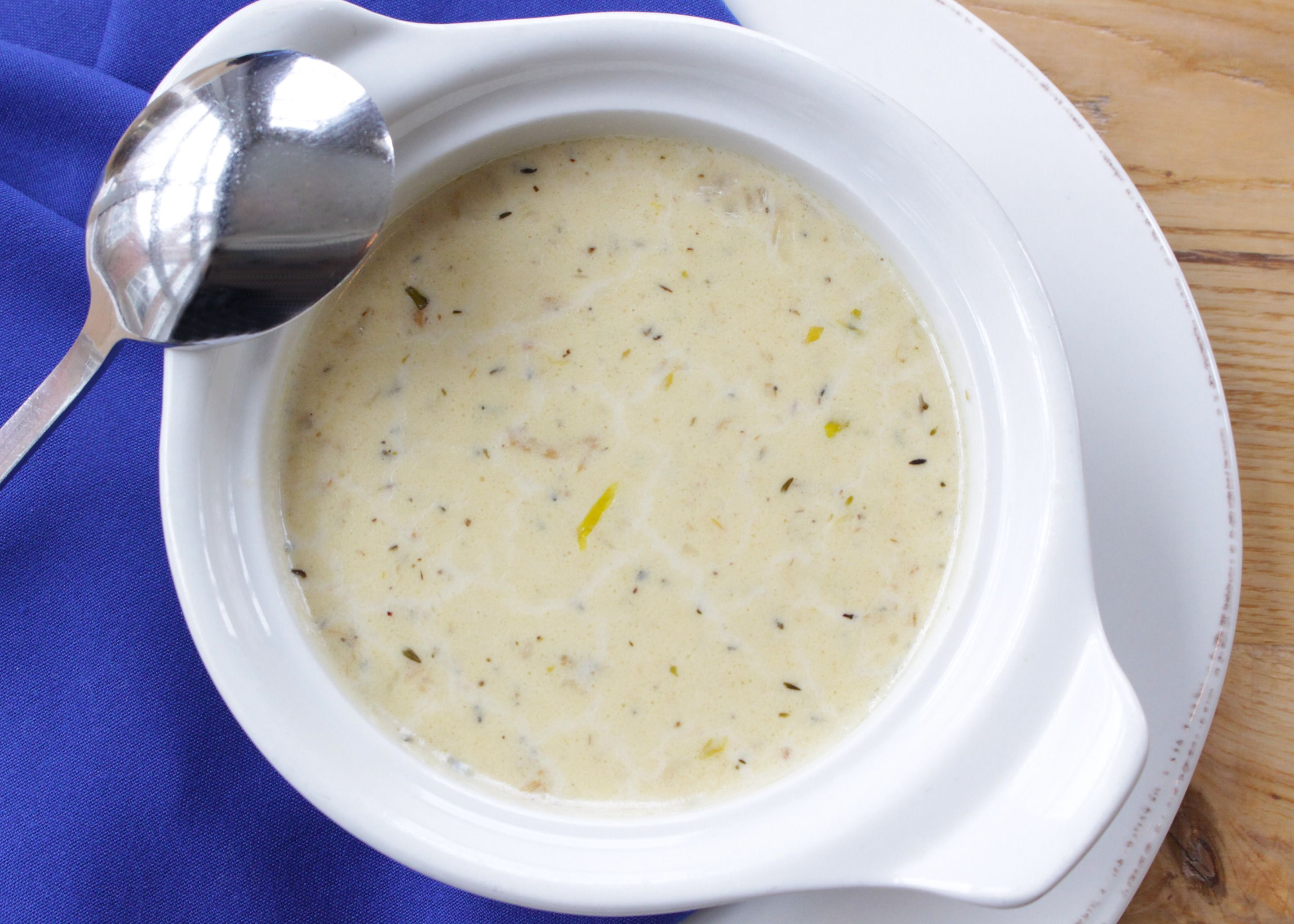 A white bowl of creamy soup with herbs, placed on a blue cloth.