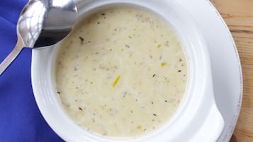 A white bowl of creamy soup with herbs, placed on a blue cloth.