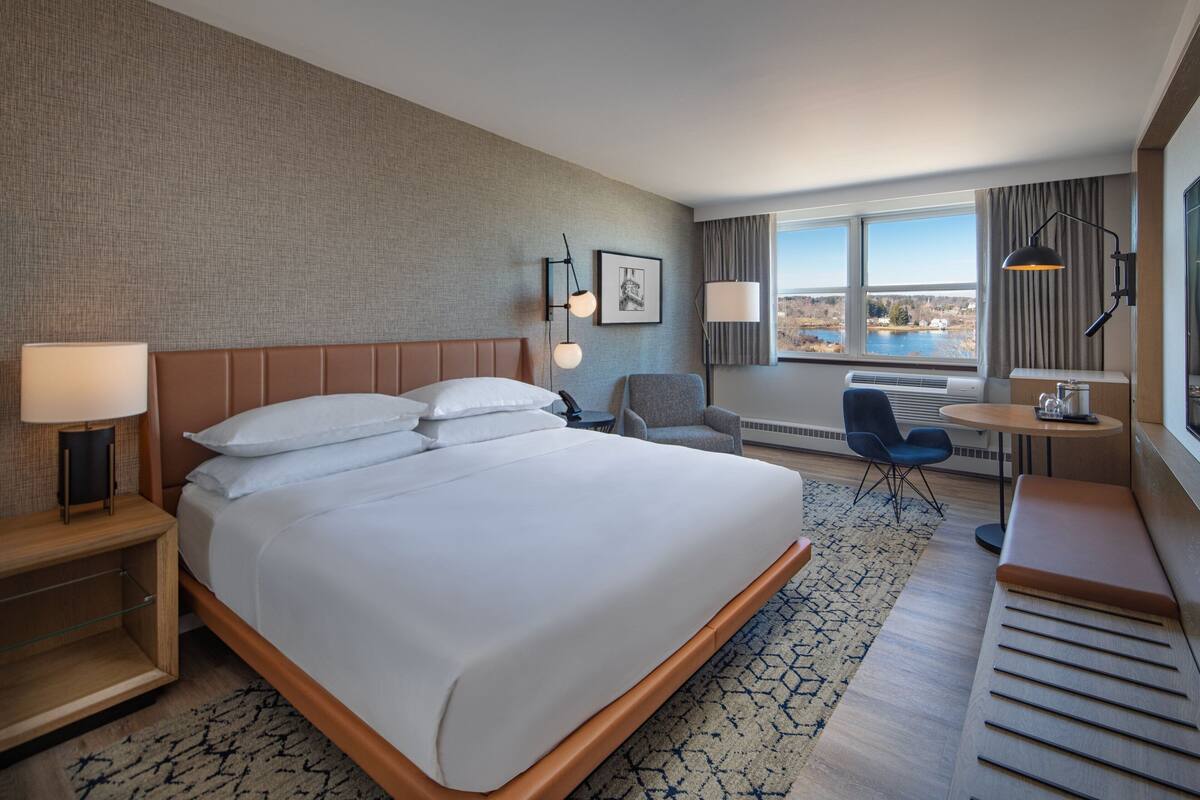 A hotel room with a large bed, a desk, a chair, and a view of the outdoors.