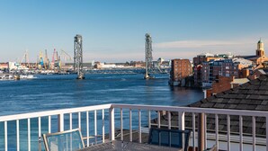 A waterfront view with a table and chairs on a balcony, overlooking a harbor with cranes and buildings. - Sheraton Portsmouth Harborside Hotel (Portsmouth)