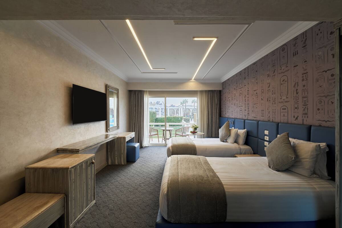 A hotel room with two beds, a desk, a flat-screen TV, and a balcony with a view.
