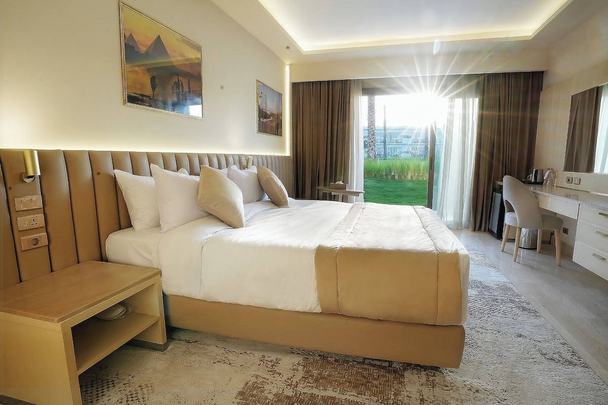 A hotel room with a large bed, a desk, a chair, a small table, and a view of the outdoors.