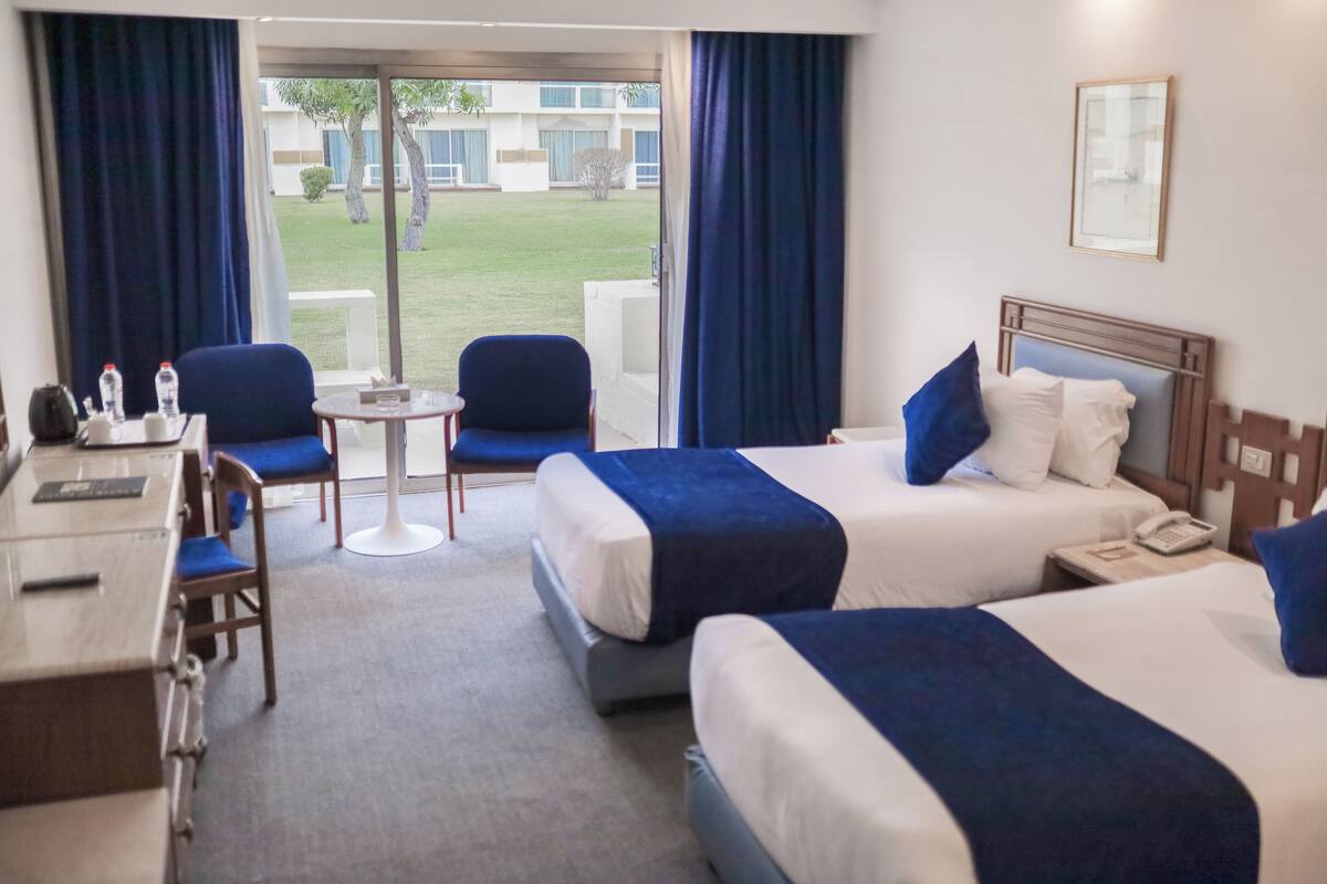 A hotel room with two beds, a desk, chairs, and a small table.