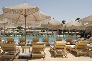 A poolside area with lounge chairs and thatched umbrellas. - Pyramids Park Resort Cairo (Giza)