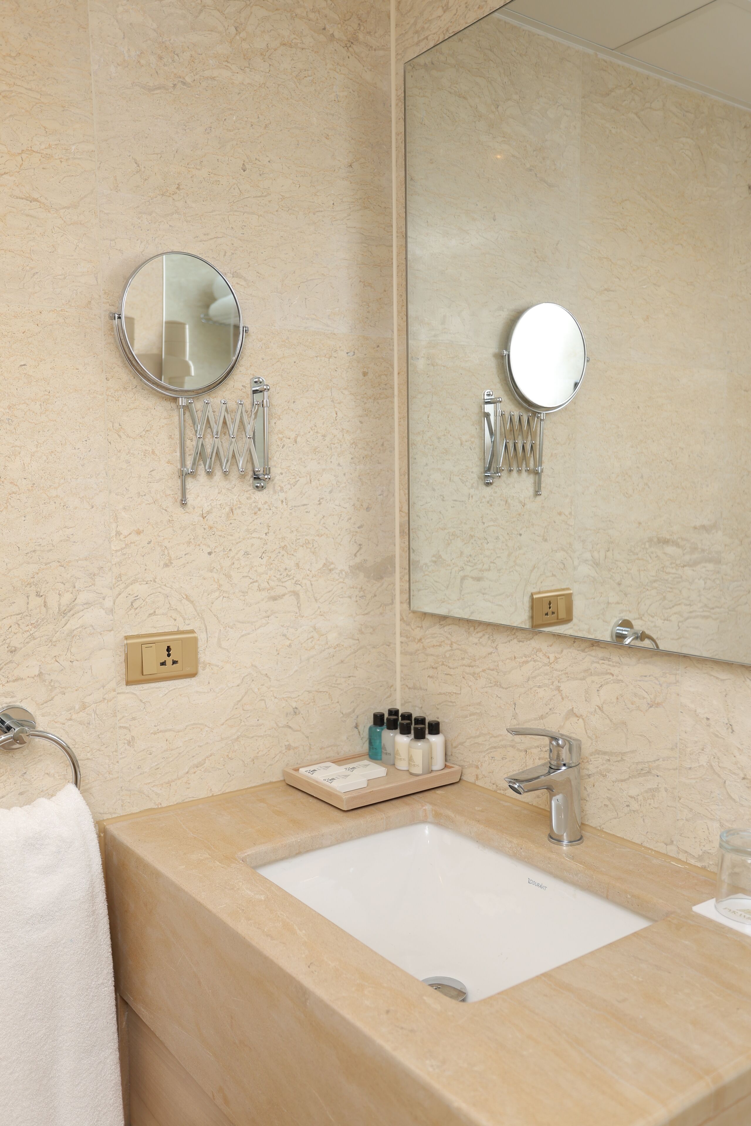 Un baño con lavamanos, espejo, perchero para toallas y artículos de aseo.