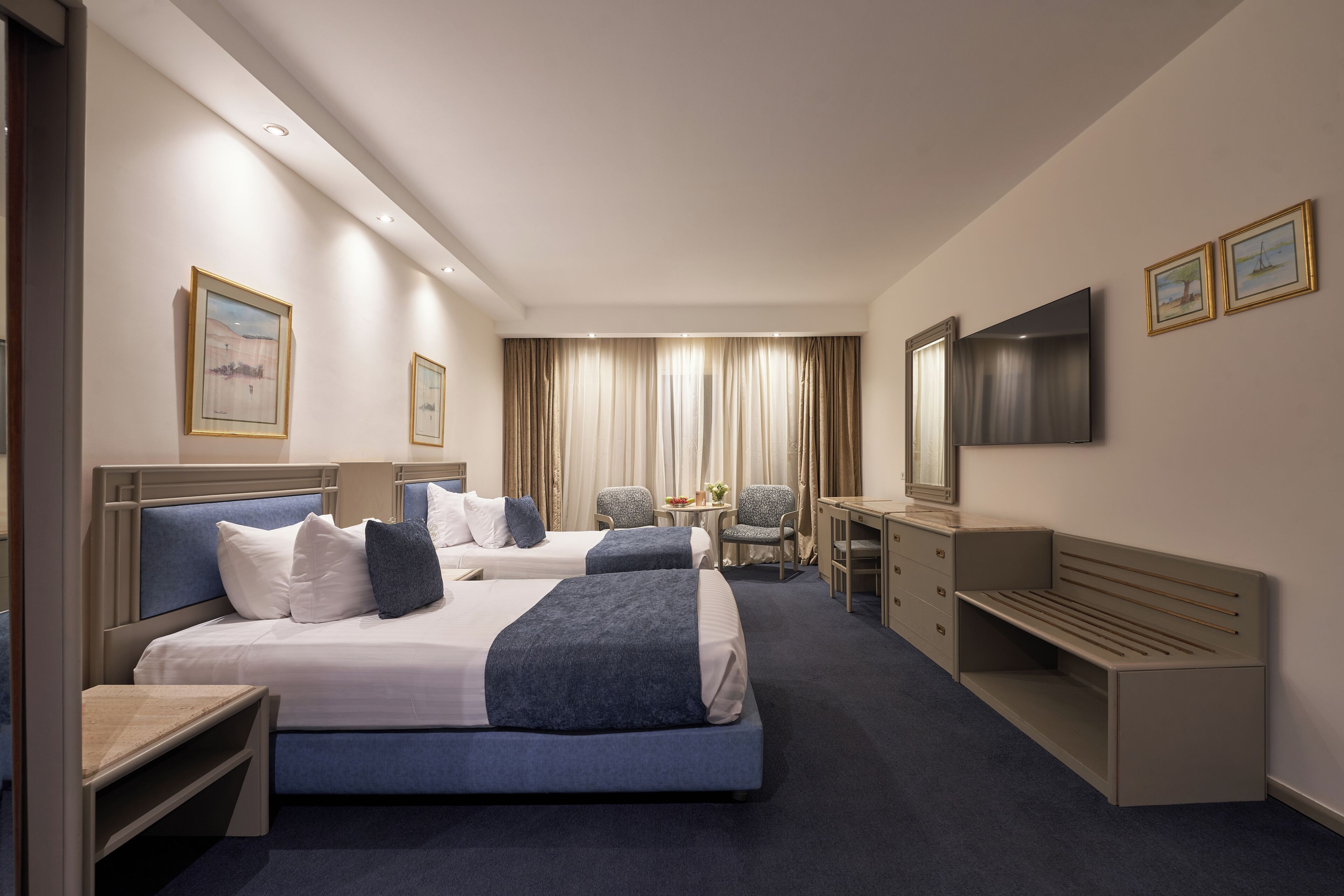 A hotel room with two beds, a desk, a chair, a TV, and a window with curtains.