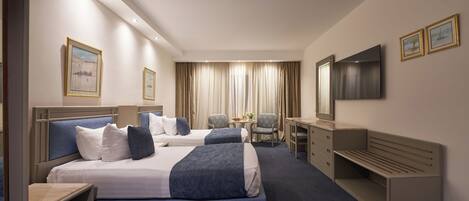 A hotel room with two beds, a desk, a chair, a TV, and a window with curtains.