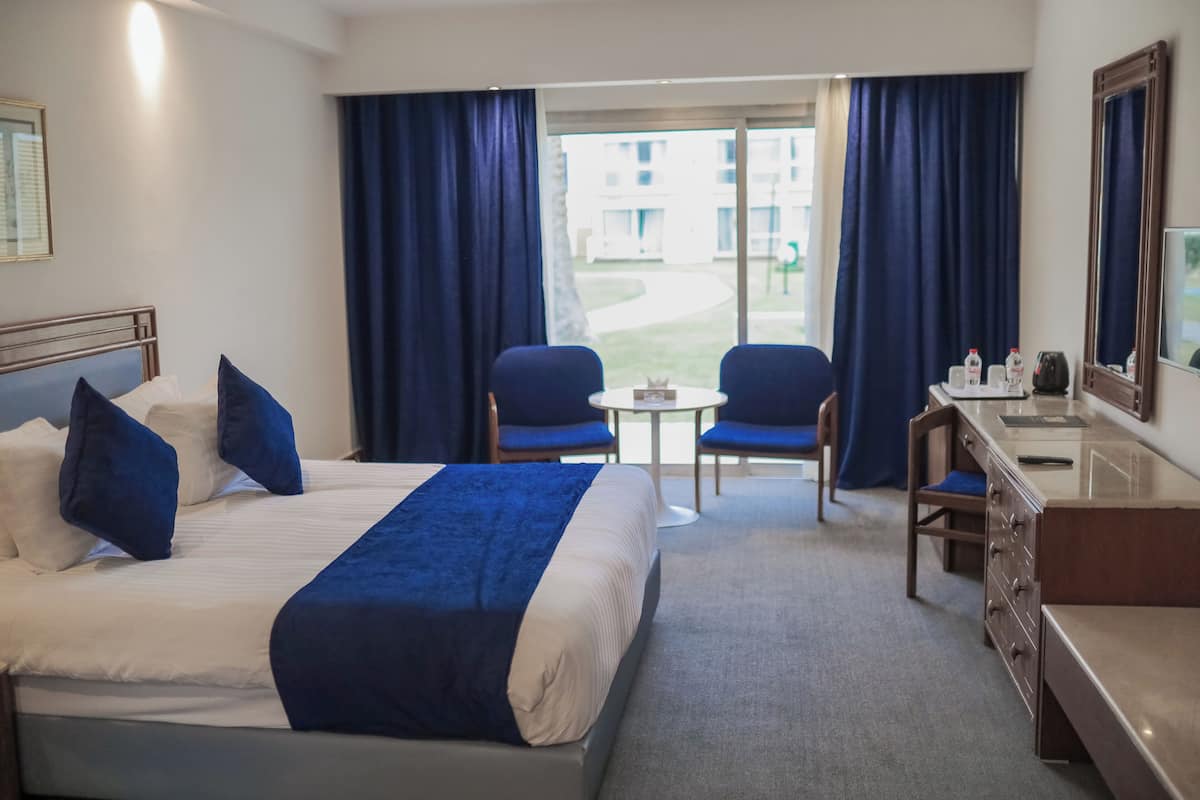 A hotel room with a bed, two chairs, a small table, a desk, and a view of the outside.