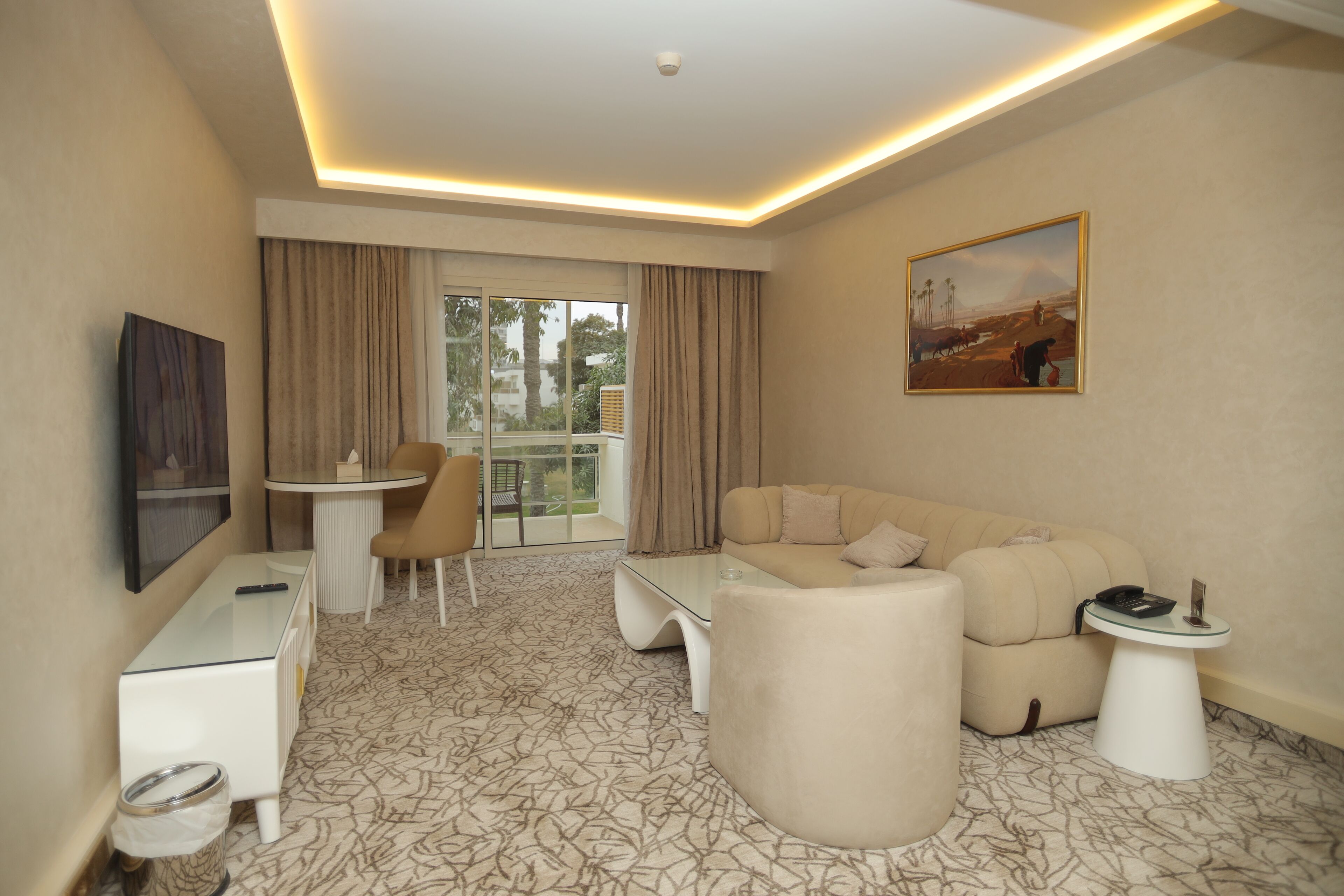 A modern hotel room with a sofa, a small table, a desk, a chair, and a balcony with curtains.