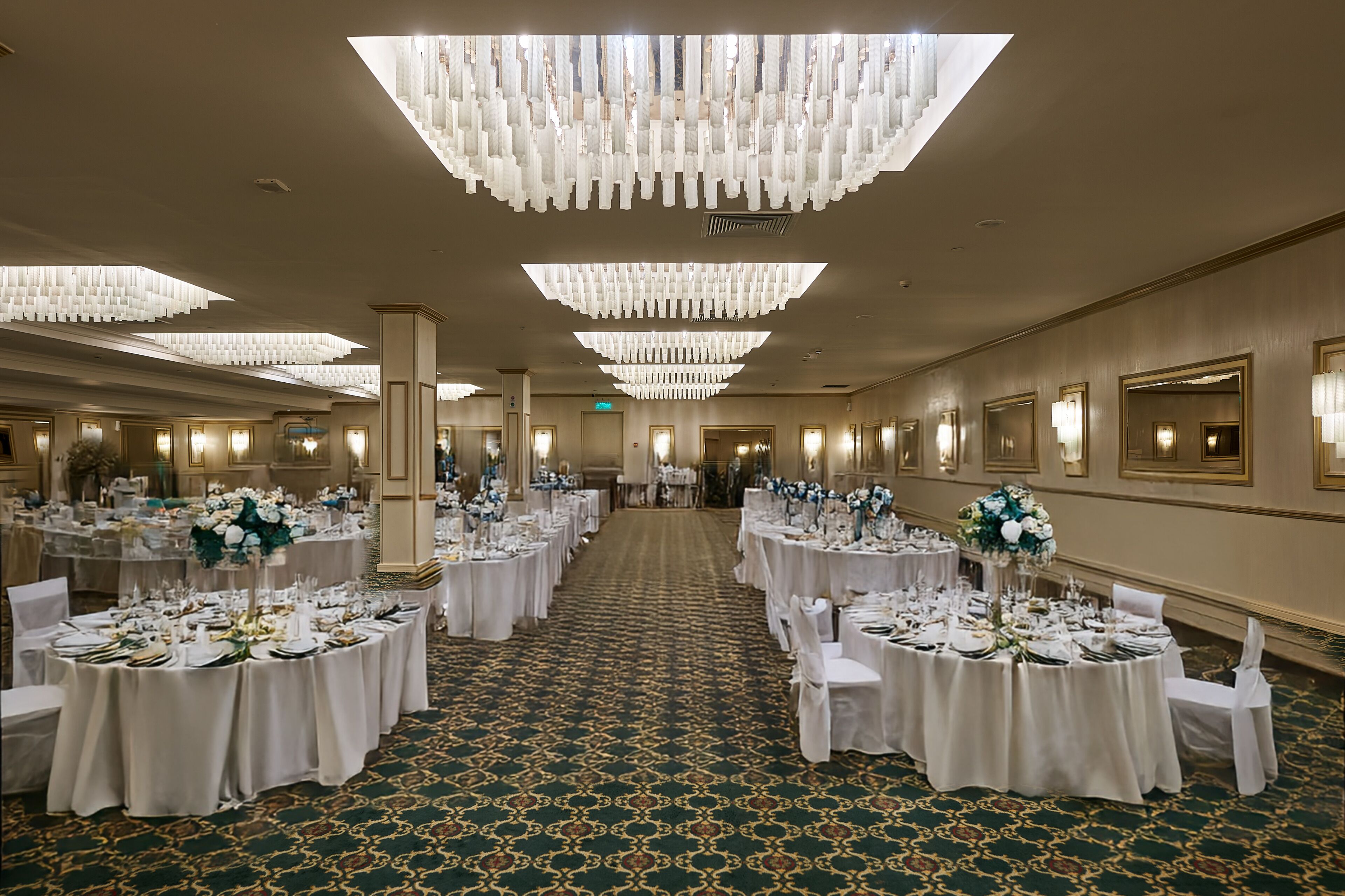 A banquet hall with round tables set for a formal event, featuring chandeliers and wall sconces.