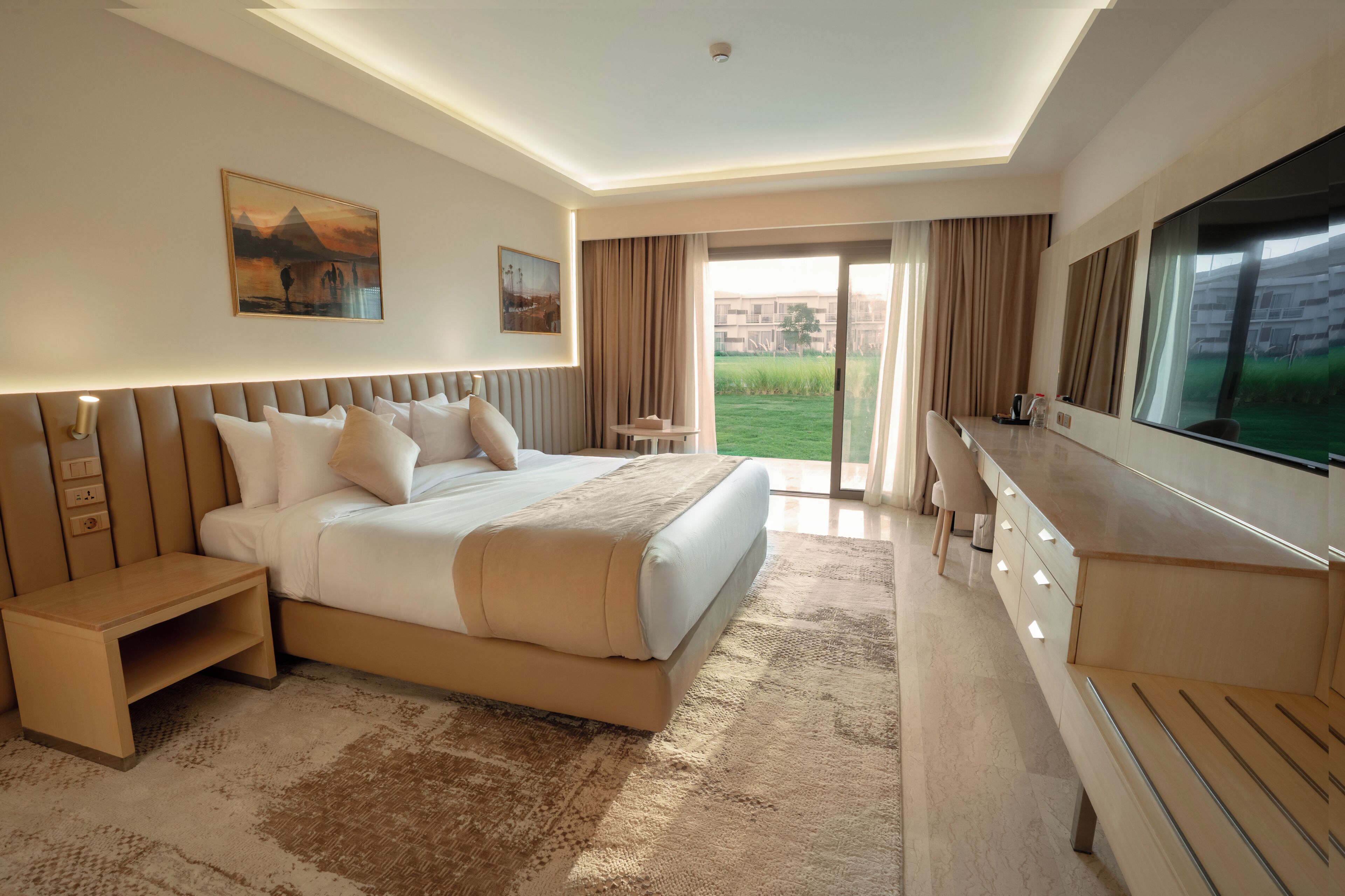 Ein Hotelzimmer mit einem großen Bett, einem Fernseher, einem Schreibtisch und Blick ins Freie.