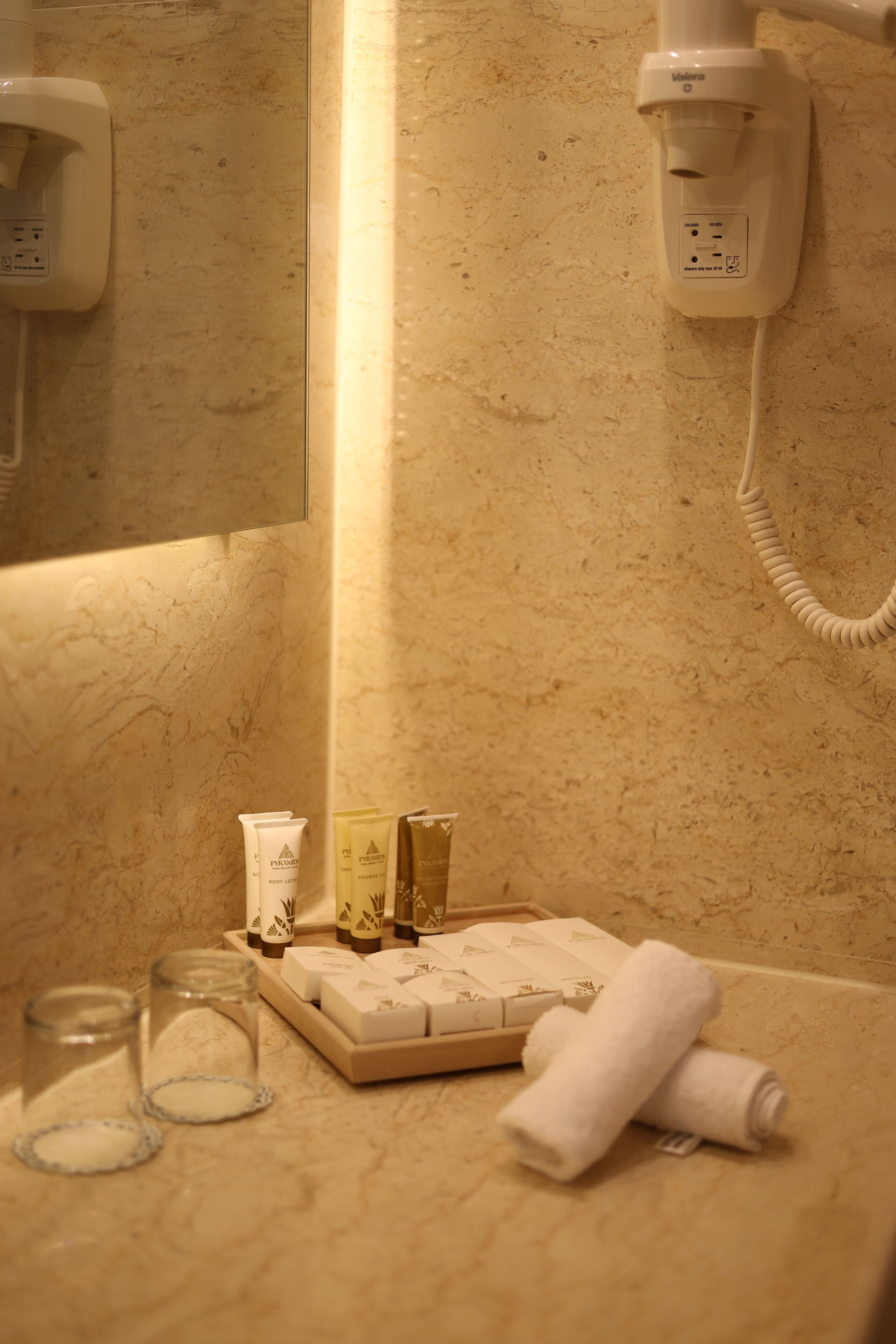 Un baño con pared de mármol, un secador de pelo, artículos de tocador y una toalla sobre el mostrador.