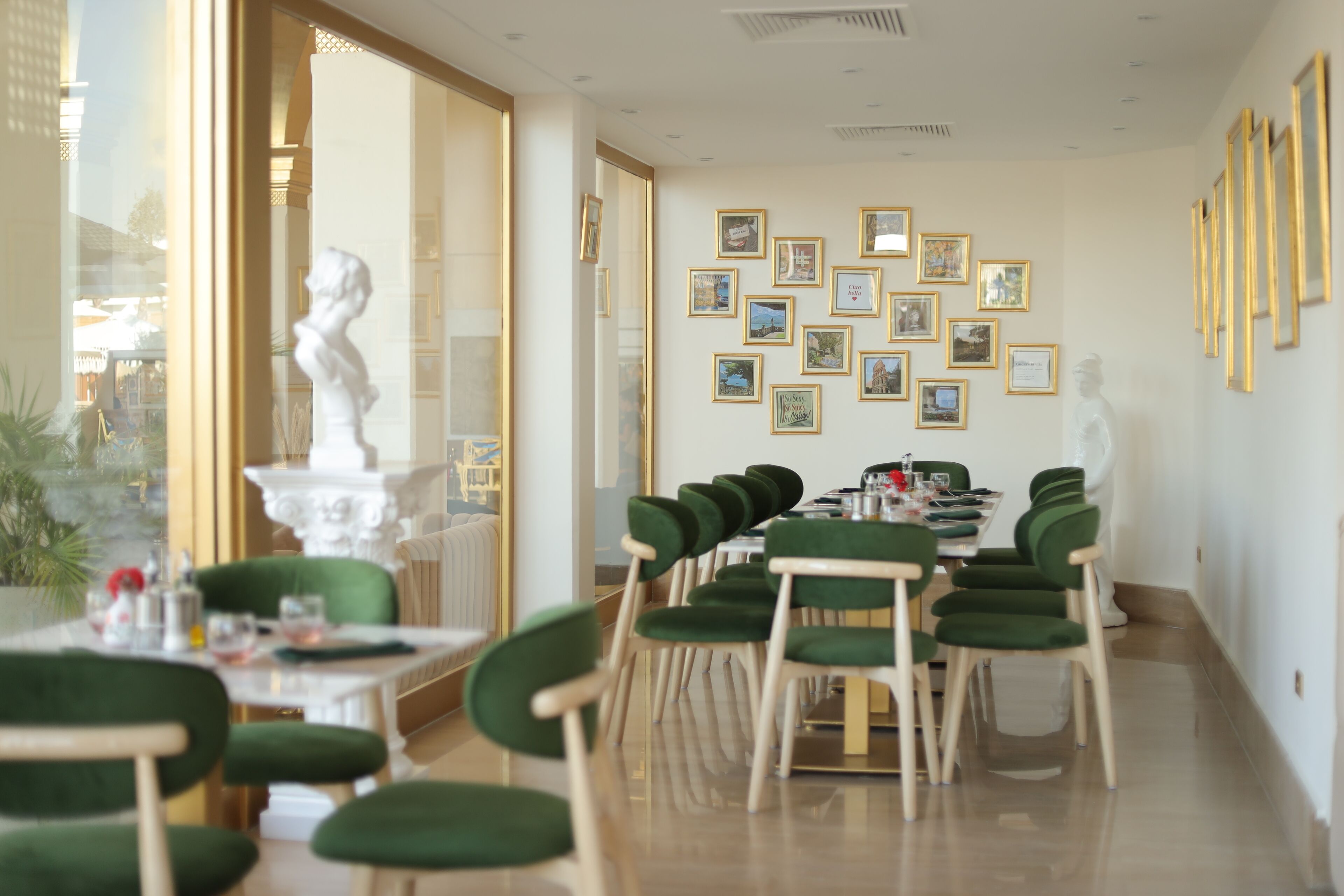 A dining area with a long table, green upholstered chairs, and framed pictures on the wall.