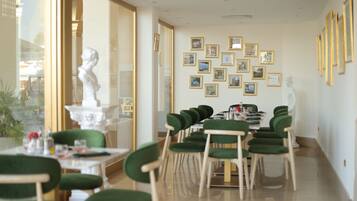 A dining area with a long table, green upholstered chairs, and framed pictures on the wall.