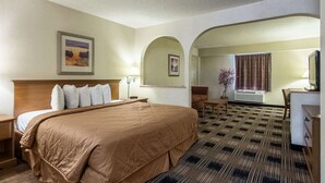 A hotel room with a large bed, a desk, a chair, a lamp, and a window with curtains. - Quality Inn Oakwood - Gainesville (Flowery Branch)