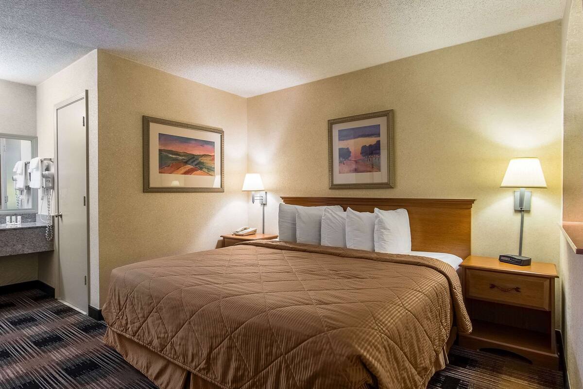 A hotel room with a large bed, two bedside lamps, a nightstand, a mirror, and two framed pictures on the wall.