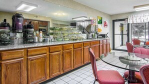 A hotel kitchen with a central island, wooden cabinets, and a glass dining area with red chairs. - Quality Inn Oakwood - Gainesville (Flowery Branch)