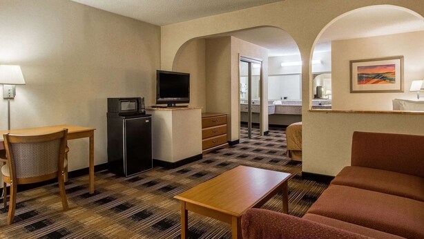 A hotel room with a kitchenette, a television, a dining table, a sofa, and a patterned carpet. - Quality Inn Oakwood - Gainesville (Flowery Branch)