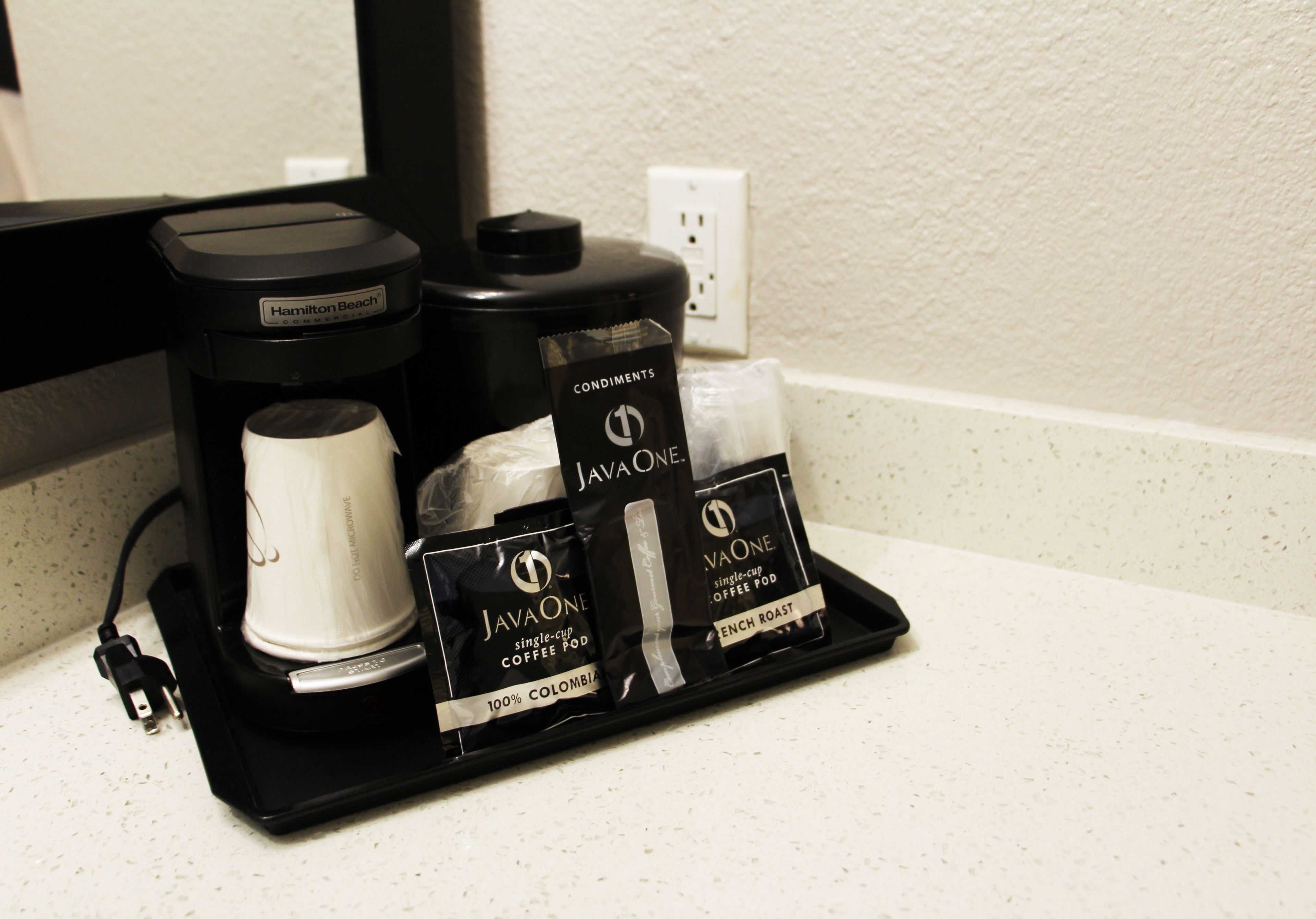 A coffee maker, a cup, and two packets of JavaOne single-cup coffee pods on a black tray.