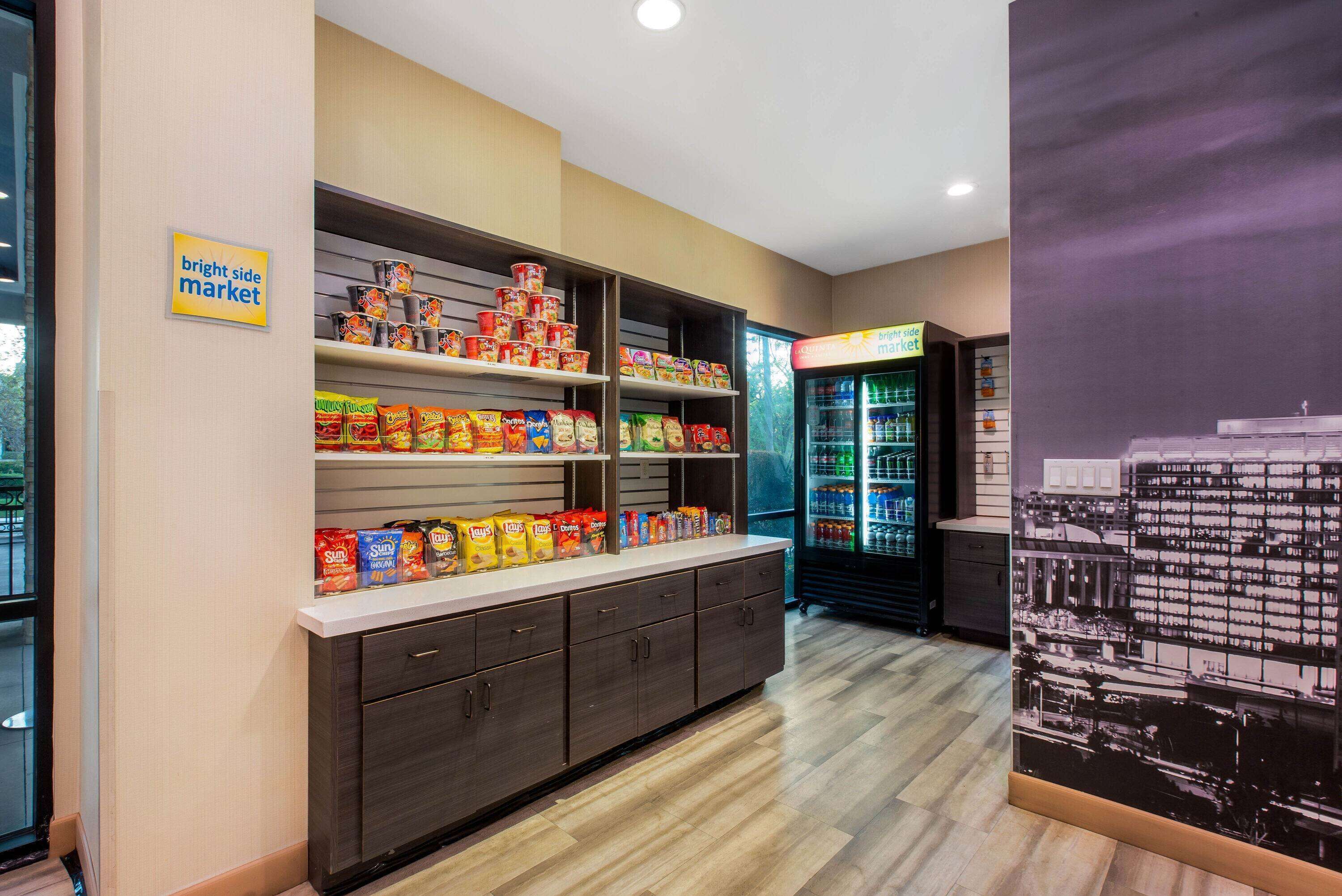 L’intérieur d’une épicerie, avec des étagères remplies de collations et de boissons, un rayon réfrigéré et une fresque représentant un paysage urbain sur le mur.