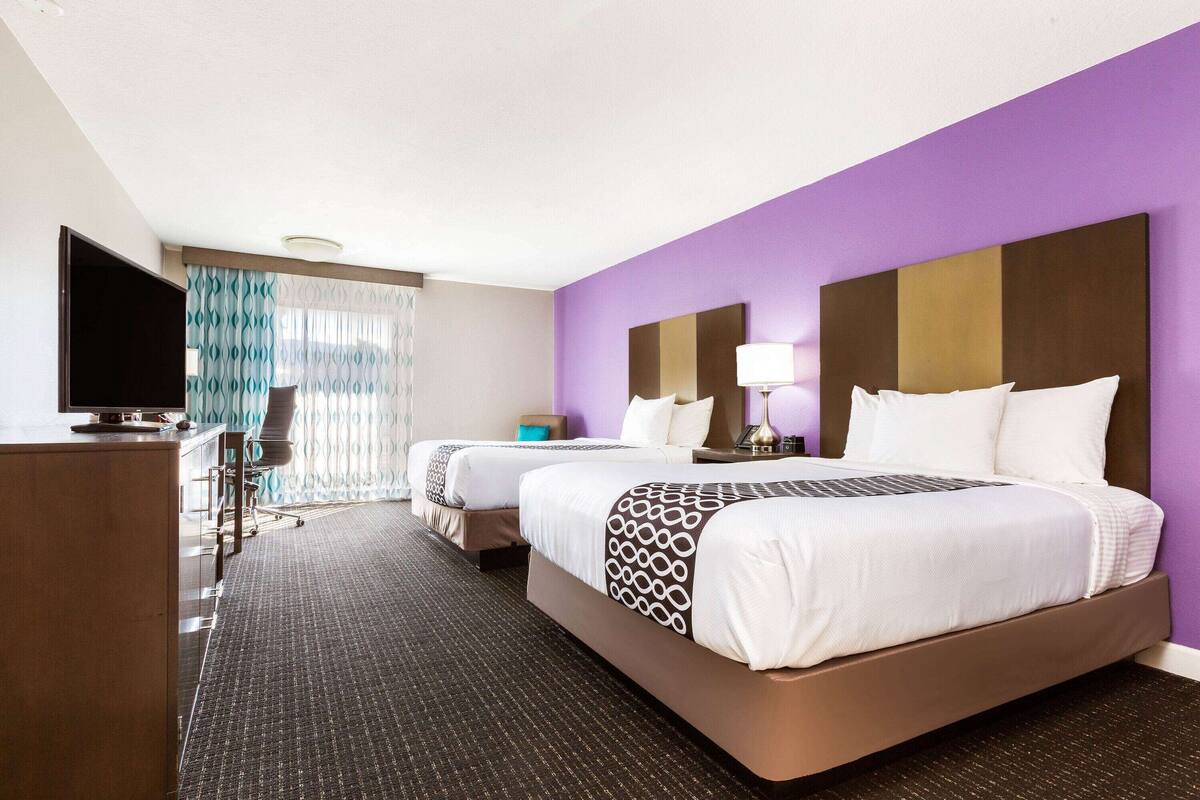Une chambre d’hôtel avec deux lits, un bureau, une télévision et une fenêtre avec des rideaux.