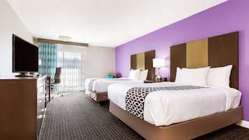 A hotel room with two beds, a desk, a TV, and a window with curtains.