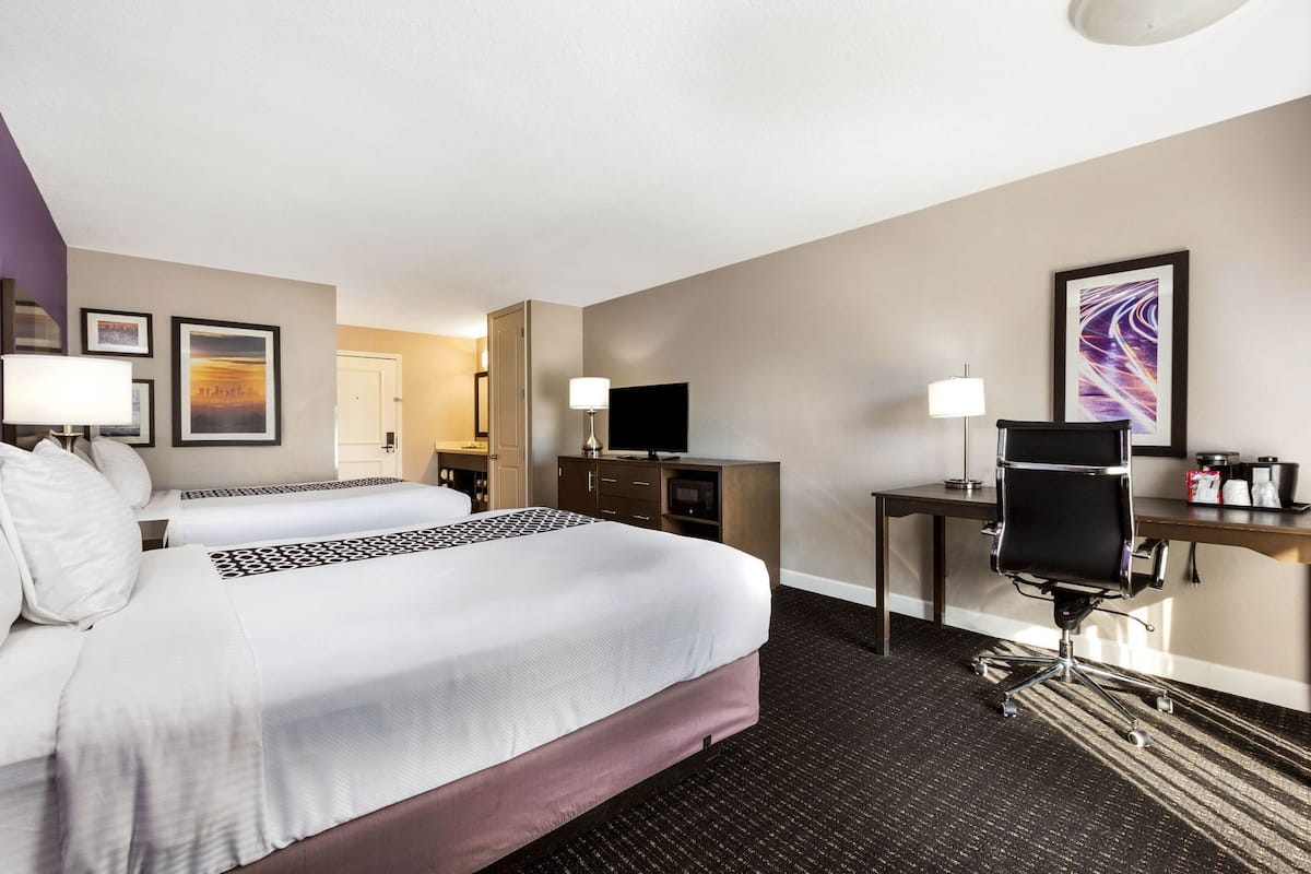 Une chambre d’hôtel avec deux lits, un bureau, une chaise, une télévision et une porte de salle de bain.
